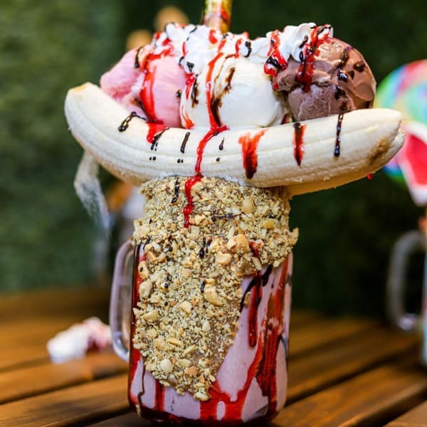 A La Crepe Og Gourmet milkshake with a banana, ice cream, whipped cream, and nuts.