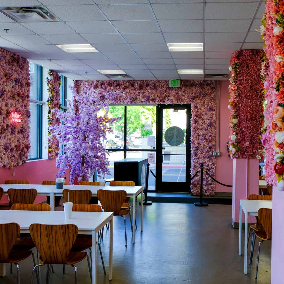 The interior of La Crepe Og Gourmet, featuring pink floral walls, white tables, and wooden chairs.