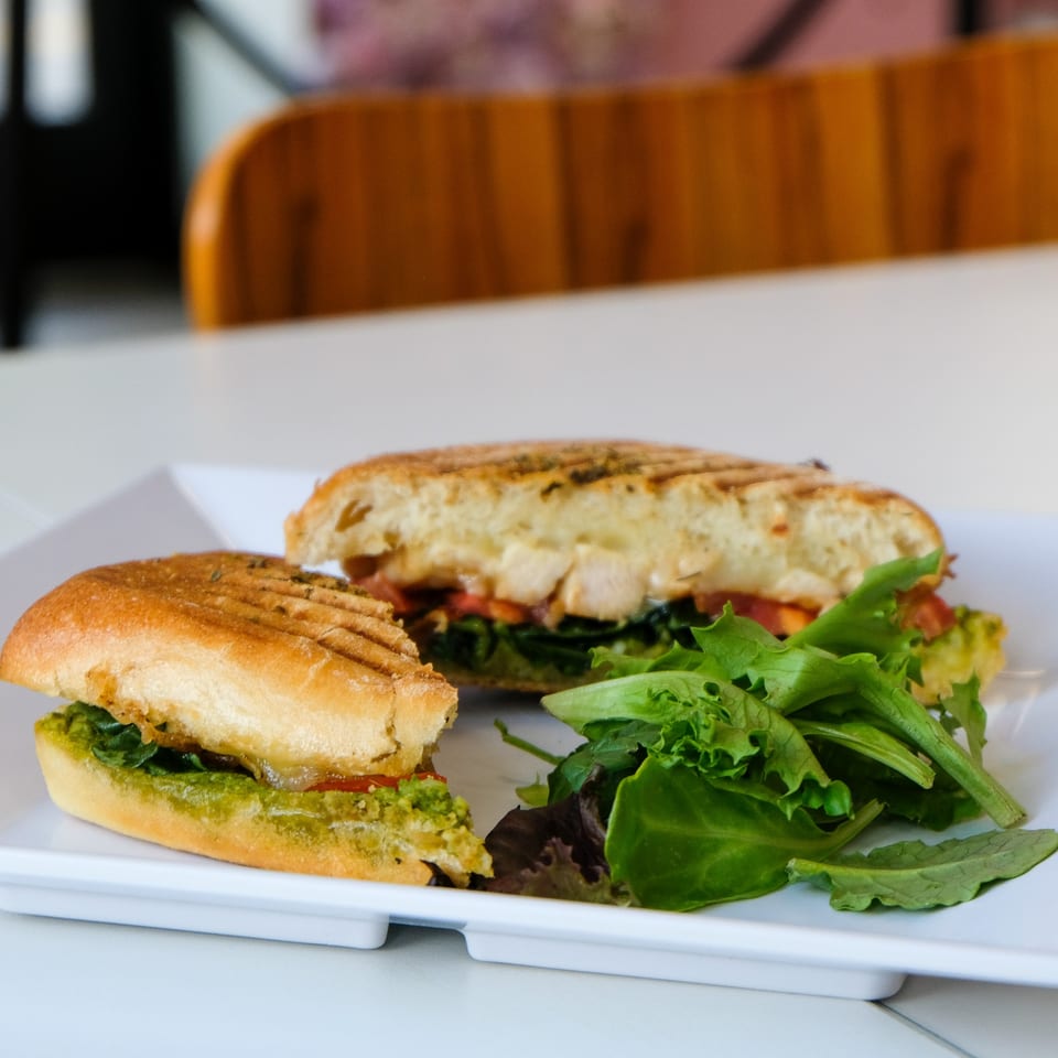Grilled panini sandwich with pesto, chicken, and salad greens on a white plate.