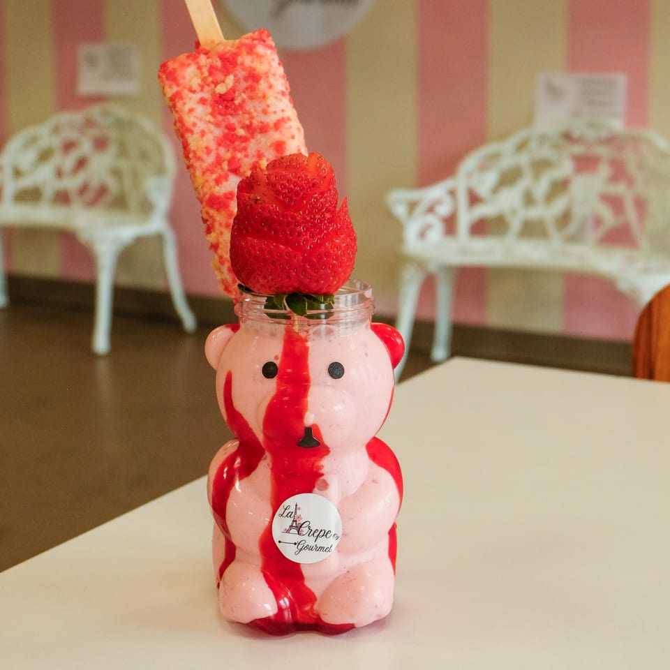Strawberry milkshake in a bear-shaped glass with a strawberry and a strawberry popsicle.