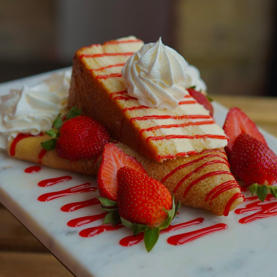 A slice of strawberry shortcake with whipped cream, surrounded by crepes, fresh strawberries, and strawberry syrup.