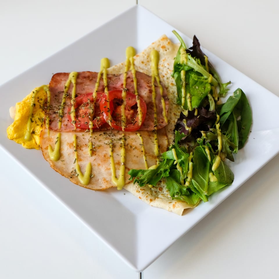 Savory La Crepe Og Gourmet crepe with ham, tomatoes, scrambled eggs, and a side salad, drizzled with sauce.
