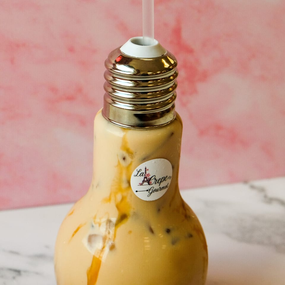 Iced coffee in a lightbulb-shaped glass with a straw and La Crepe Og Gourmet logo.