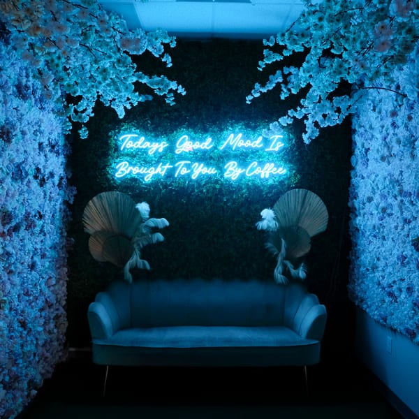 A neon sign reading "Today's Good Mood Is Brought To You By Coffee" above a blue couch.