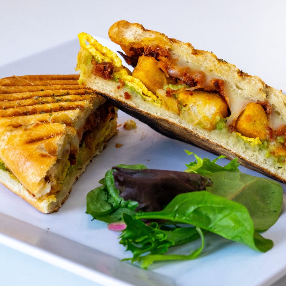 A La Crepe Og Gourmet panini, cut in half, filled with eggs, potatoes, and chorizo, served with a side salad.