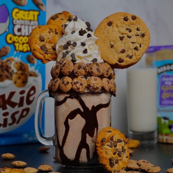 A chocolate milkshake in a mug, topped with whipped cream, chocolate chips, and cookies.