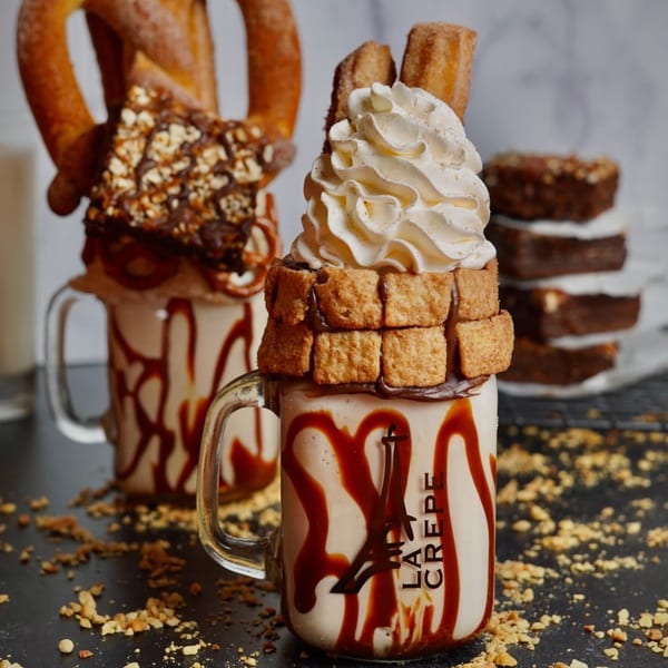Two La Crepe Og Gourmet milkshakes with pretzels, brownies, churros, and whipped cream.