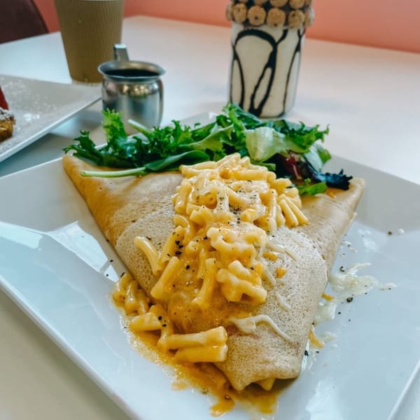 Savory crepe filled with macaroni and cheese, topped with fresh greens, on a white plate.